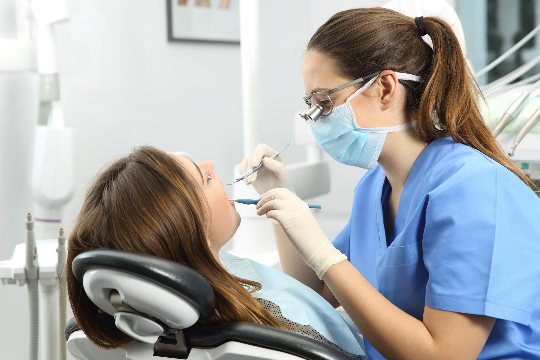 Dentist wearing eyeglasses gloves and mask examining a patient teeth