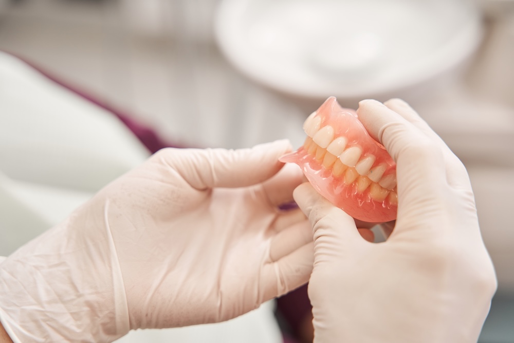 Cropped view of the dentist holding dentures in her hands.